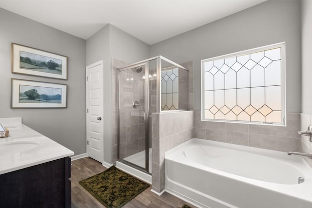 bathroom featuring wood finished floors, vanity, baseboards, a bath, and a stall shower