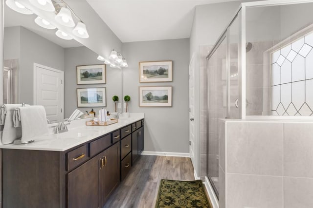 bathroom with wood finished floors, a sink, baseboards, double vanity, and a stall shower