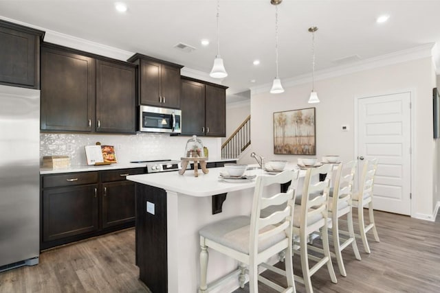 kitchen with dark brown cabinetry, decorative light fixtures, light countertops, appliances with stainless steel finishes, and a center island with sink