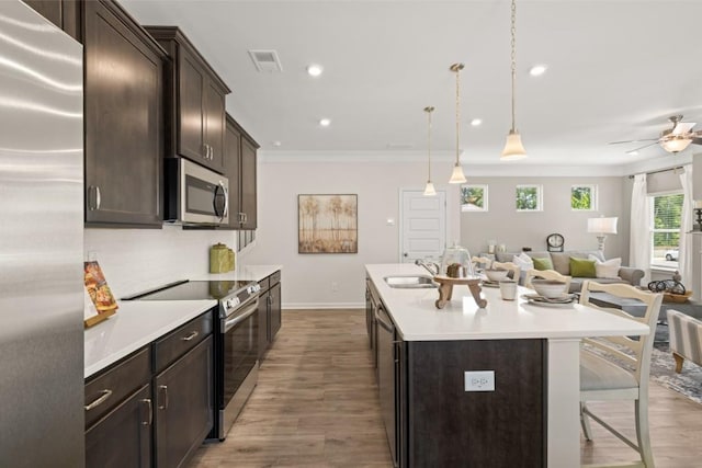 kitchen with open floor plan, hanging light fixtures, a kitchen island with sink, stainless steel appliances, and light countertops