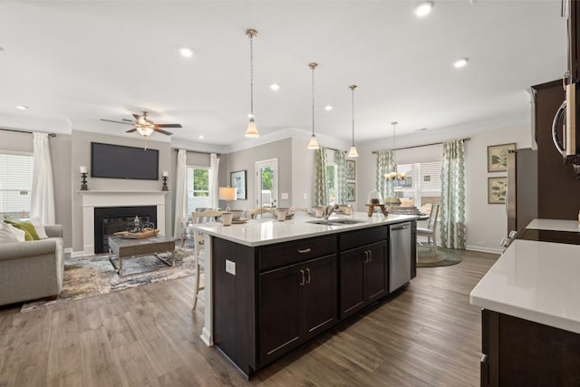 kitchen with open floor plan, hanging light fixtures, a kitchen island with sink, stainless steel appliances, and light countertops