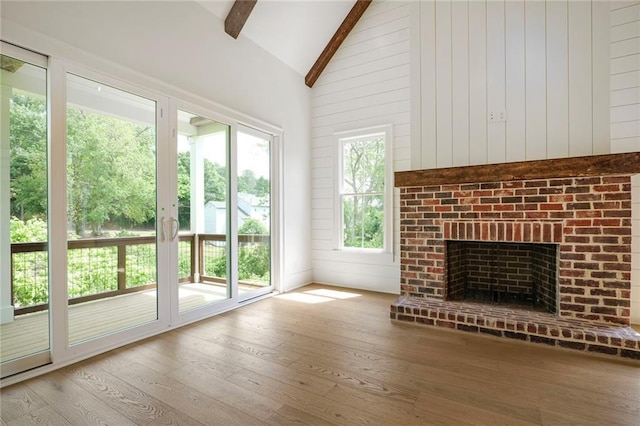 unfurnished living room featuring beam ceiling, wood finished floors, a fireplace, wooden walls, and high vaulted ceiling