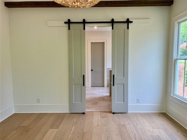 spare room featuring light wood-type flooring, a barn door, plenty of natural light, and baseboards