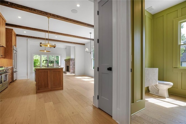 kitchen with plenty of natural light, light wood-style floors, brown cabinets, beam ceiling, and recessed lighting