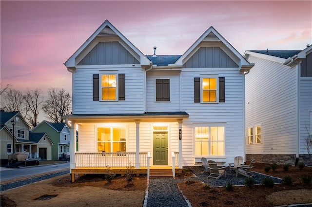 back of house at dusk featuring a porch and board and batten siding