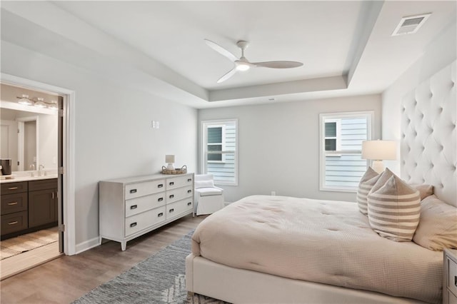 bedroom featuring light wood-type flooring, a tray ceiling, visible vents, and a sink