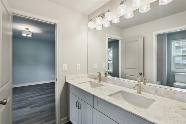 full bathroom with double vanity, a sink, toilet, and baseboards