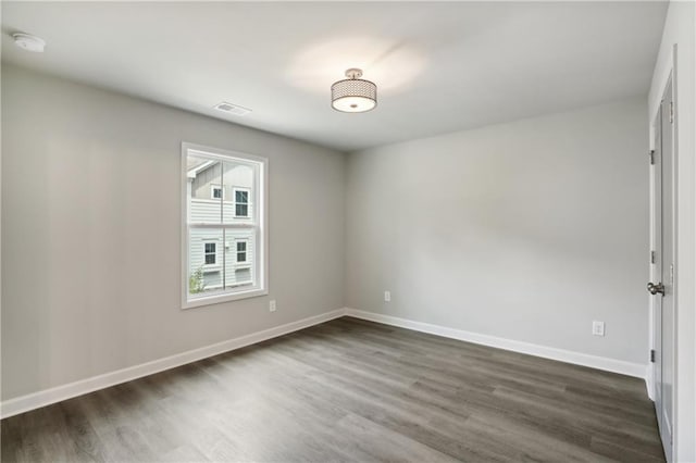 unfurnished room featuring dark wood-style floors, visible vents, and baseboards