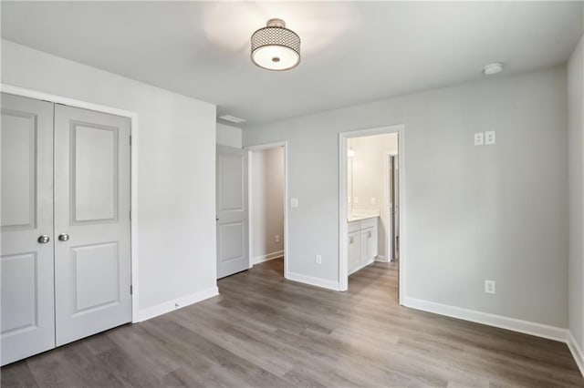 unfurnished bedroom with a closet, ensuite bath, baseboards, and wood finished floors