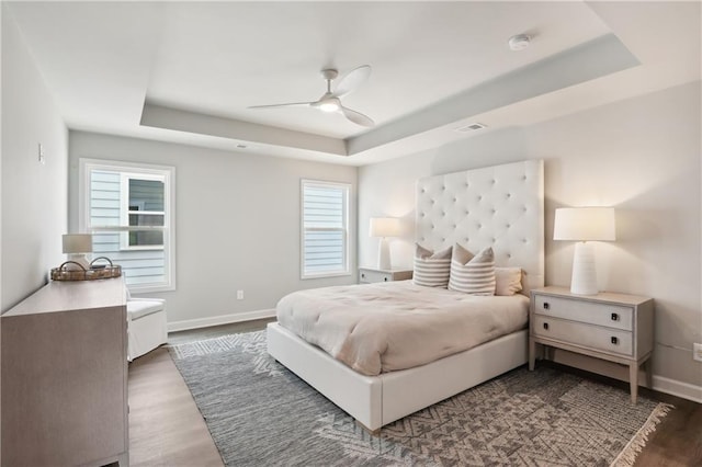 bedroom with baseboards, visible vents, ceiling fan, wood finished floors, and a tray ceiling