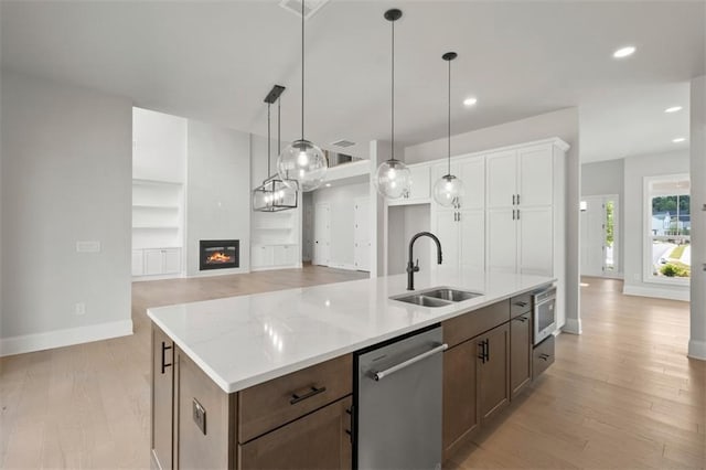 kitchen with sink, a kitchen island with sink, white cabinetry, a large fireplace, and stainless steel dishwasher