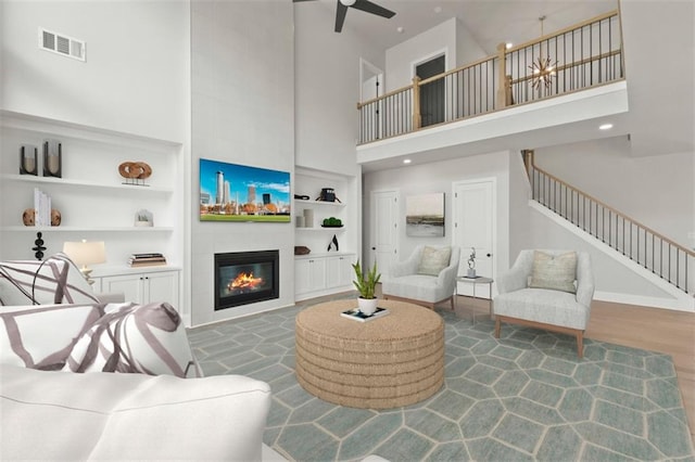 living room with a towering ceiling, dark hardwood / wood-style floors, a large fireplace, ceiling fan, and built in shelves