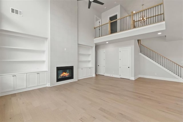 unfurnished living room with light hardwood / wood-style flooring, a tiled fireplace, a high ceiling, ceiling fan, and built in shelves