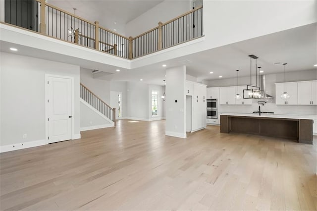 unfurnished living room with sink, light hardwood / wood-style flooring, and a high ceiling