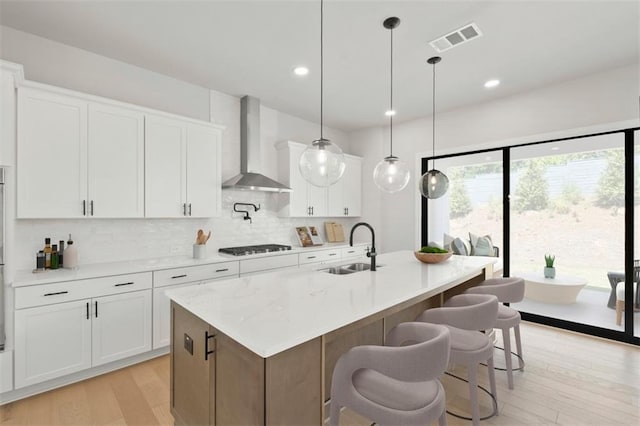 kitchen featuring white cabinetry, a kitchen island with sink, and wall chimney range hood