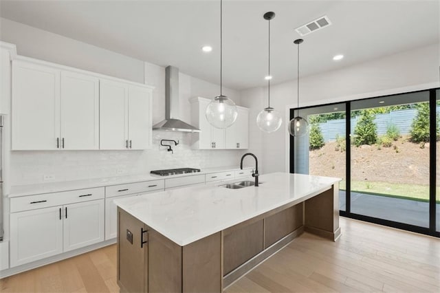 kitchen with a kitchen island with sink, white cabinets, sink, and wall chimney exhaust hood