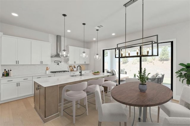 kitchen featuring sink, wall chimney range hood, an island with sink, and white cabinets