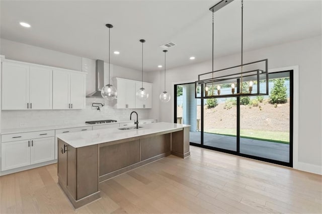 kitchen featuring wall chimney range hood, a kitchen island with sink, sink, and white cabinets