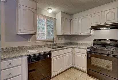 kitchen with sink, light tile patterned floors, black appliances, light stone countertops, and white cabinets