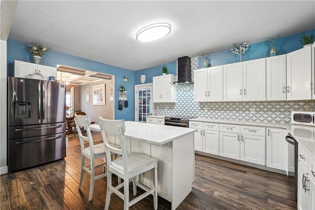 kitchen featuring dark wood-style floors, stainless steel appliances, light countertops, a kitchen breakfast bar, and wall chimney exhaust hood