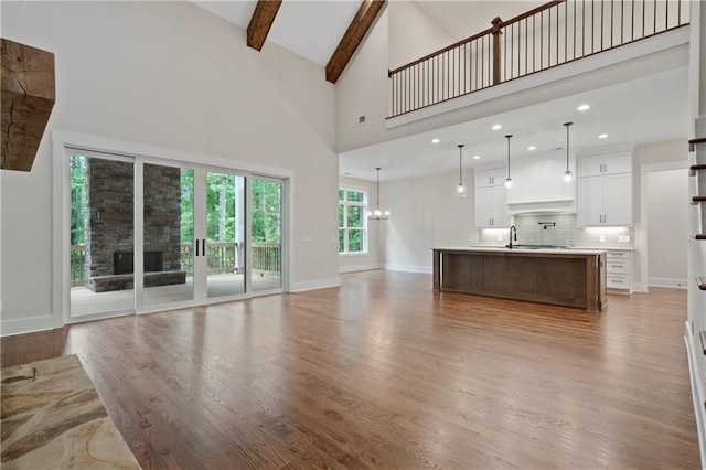 unfurnished living room featuring baseboards, an inviting chandelier, a fireplace, beamed ceiling, and light wood-type flooring