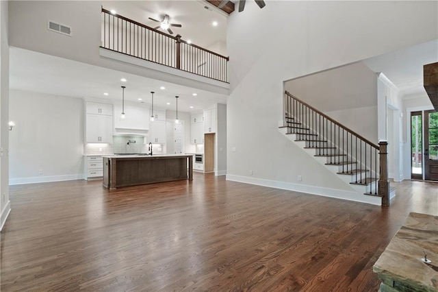 unfurnished living room featuring visible vents, baseboards, ceiling fan, stairs, and dark wood-style flooring