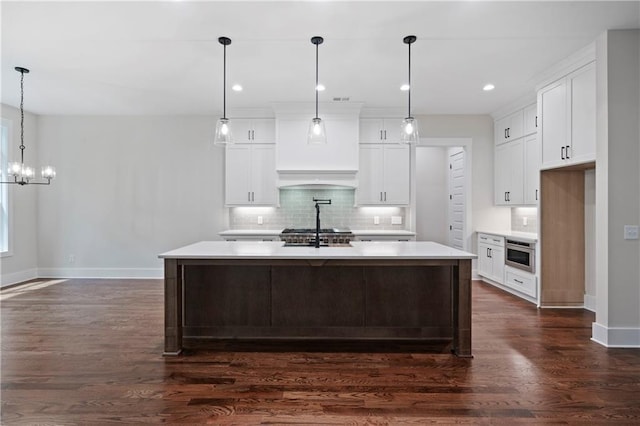 kitchen featuring dark wood-type flooring, a kitchen island with sink, tasteful backsplash, white cabinetry, and light countertops