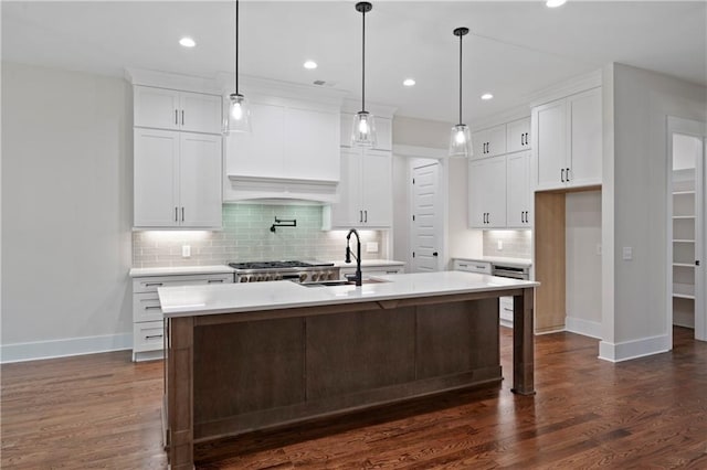 kitchen featuring a sink, an island with sink, custom range hood, white cabinets, and dark wood-style flooring