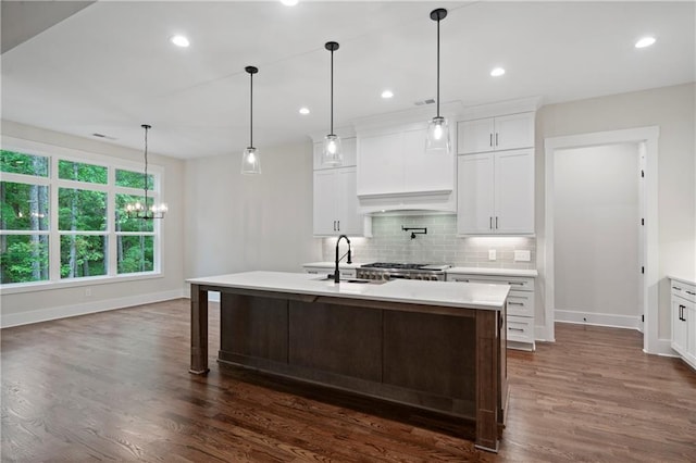 kitchen with tasteful backsplash, an island with sink, light countertops, dark wood-style floors, and a sink