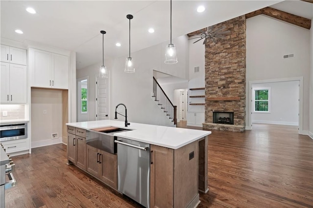 kitchen featuring dishwasher, a stone fireplace, dark wood finished floors, and a sink