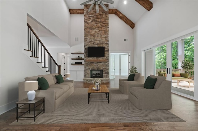 living area featuring wood finished floors, visible vents, beam ceiling, a stone fireplace, and stairs