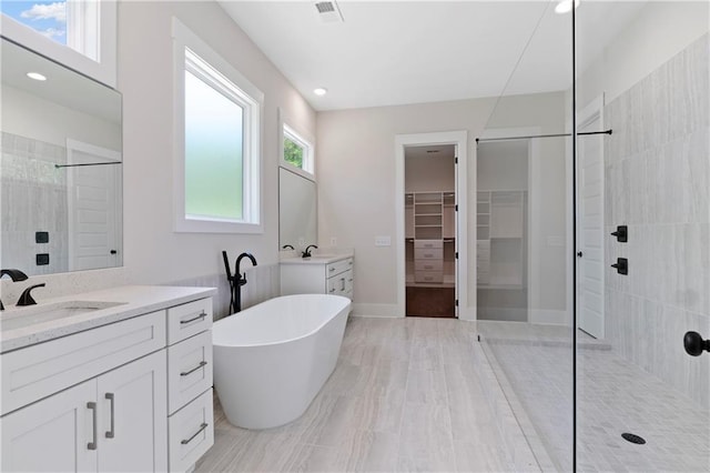 bathroom featuring visible vents, a walk in shower, two vanities, a soaking tub, and a sink