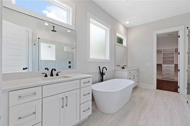 full bath featuring a sink, tiled shower, two vanities, and a wealth of natural light