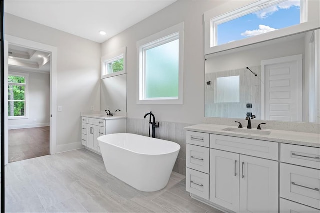 bathroom with a wealth of natural light, two vanities, a tile shower, and a sink