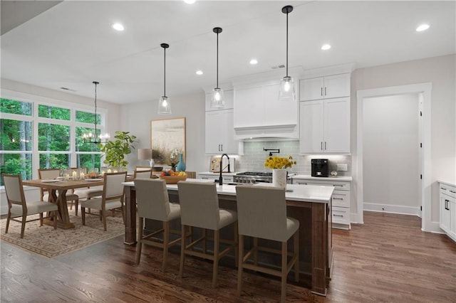 kitchen featuring dark wood-type flooring, backsplash, a center island with sink, and light countertops