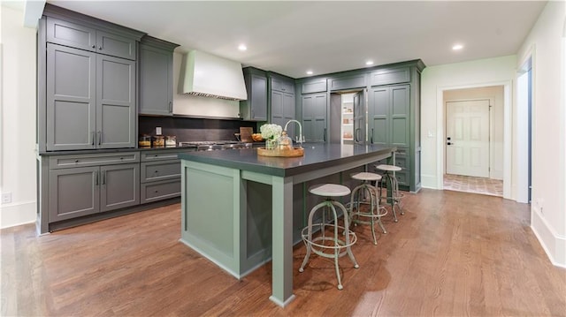 kitchen featuring gray cabinets, custom exhaust hood, a kitchen breakfast bar, wood-type flooring, and a center island with sink