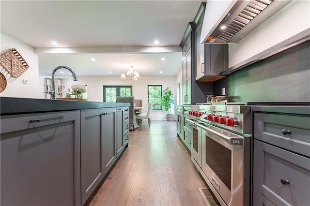 kitchen with light wood-type flooring, designer range, range hood, sink, and an inviting chandelier