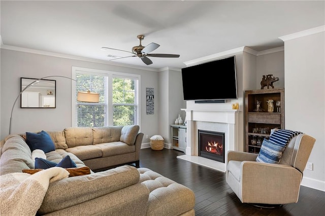 living room featuring a ceiling fan, a lit fireplace, crown molding, dark wood-type flooring, and baseboards