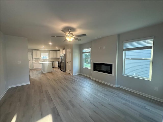 11045 Shadow Creek Ter, Hampton, GA 30228 - unfurnished living room featuring baseboards, light wood-style flooring, a glass covered fireplace, a ceiling fan, and recessed lighting