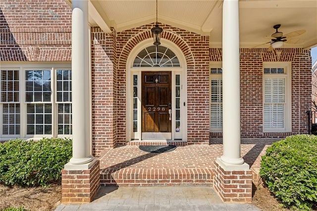 entrance to property featuring brick siding, covered porch, and ceiling fan