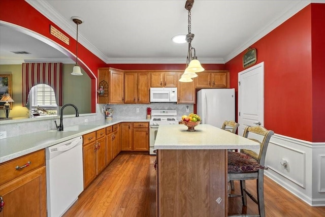 kitchen with white appliances, wood finished floors, light countertops, a kitchen bar, and a sink