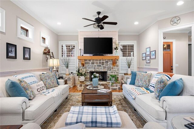 living room with recessed lighting, wood finished floors, a stone fireplace, and ornamental molding