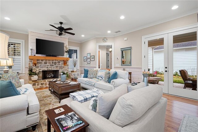 living area featuring wood finished floors, recessed lighting, a stone fireplace, french doors, and crown molding