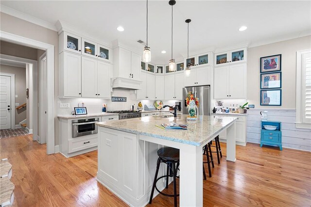 kitchen featuring a sink, stainless steel appliances, custom range hood, a kitchen breakfast bar, and light wood-type flooring