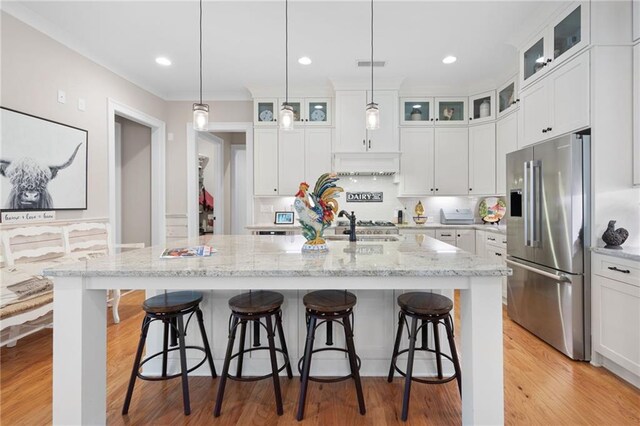 kitchen featuring pendant lighting, light wood-type flooring, light stone counters, high end fridge, and white cabinetry