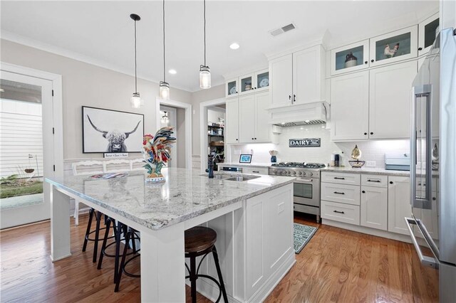 kitchen featuring visible vents, a sink, custom range hood, white cabinets, and high quality appliances