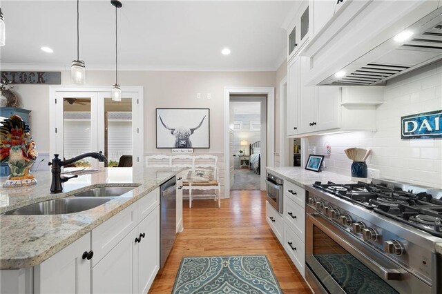 kitchen featuring light wood finished floors, custom exhaust hood, a sink, decorative backsplash, and appliances with stainless steel finishes