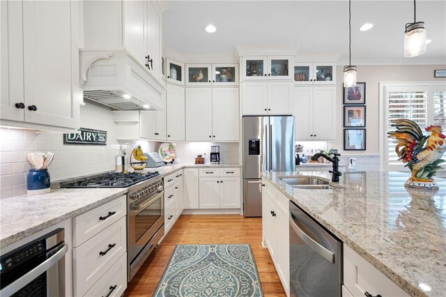 kitchen featuring light wood finished floors, glass insert cabinets, appliances with stainless steel finishes, custom exhaust hood, and a sink