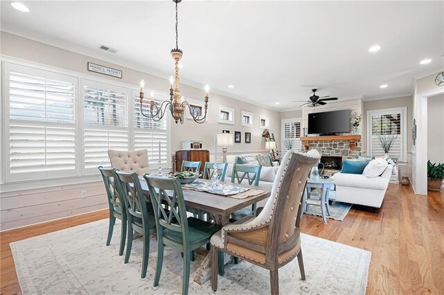 dining space featuring visible vents, light wood finished floors, a fireplace, ornamental molding, and ceiling fan with notable chandelier