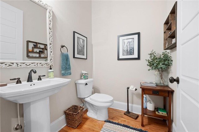 half bath with a sink, baseboards, toilet, and wood finished floors